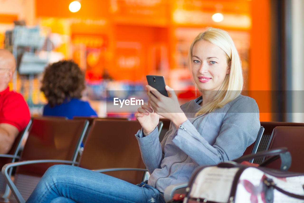 Portrait of young woman using smart phone sitting at airport
