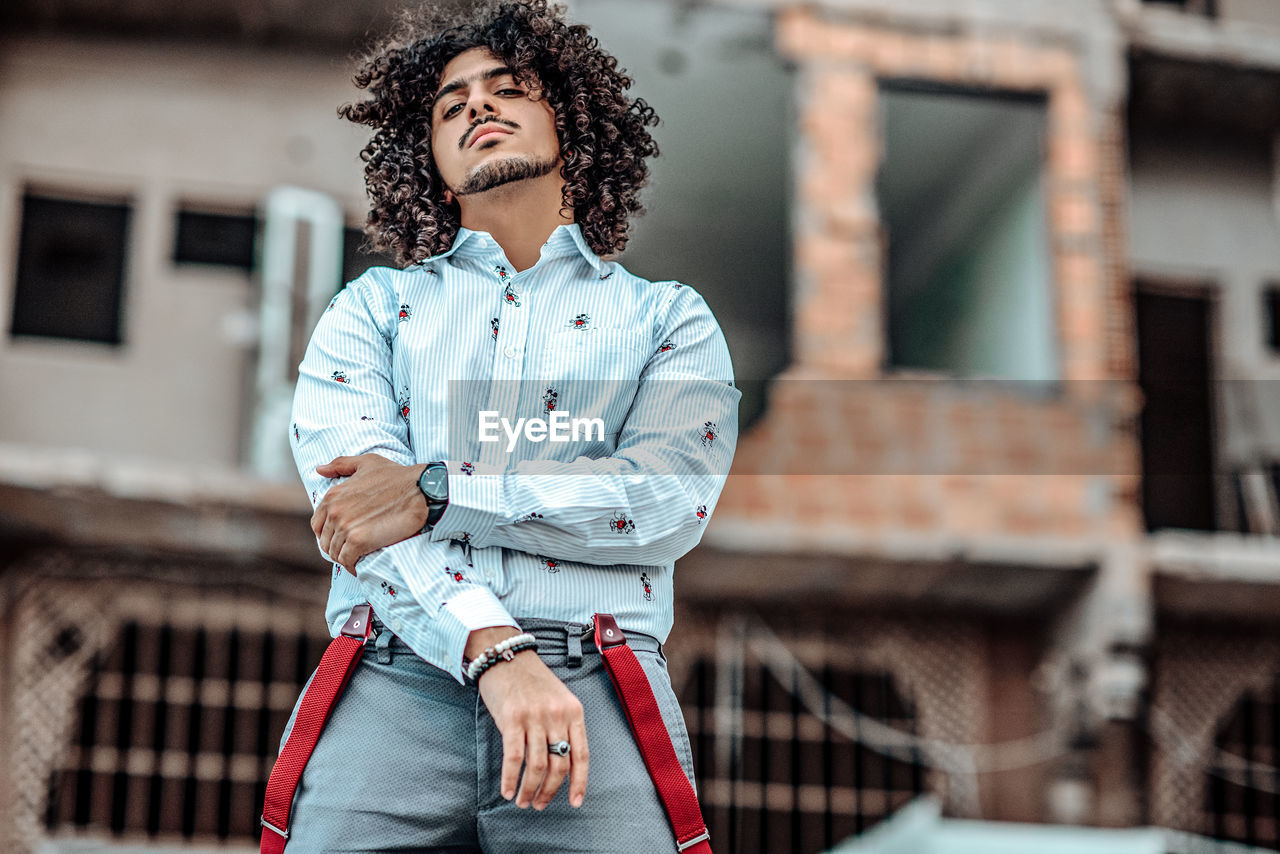 Young man looking away while standing against built structure