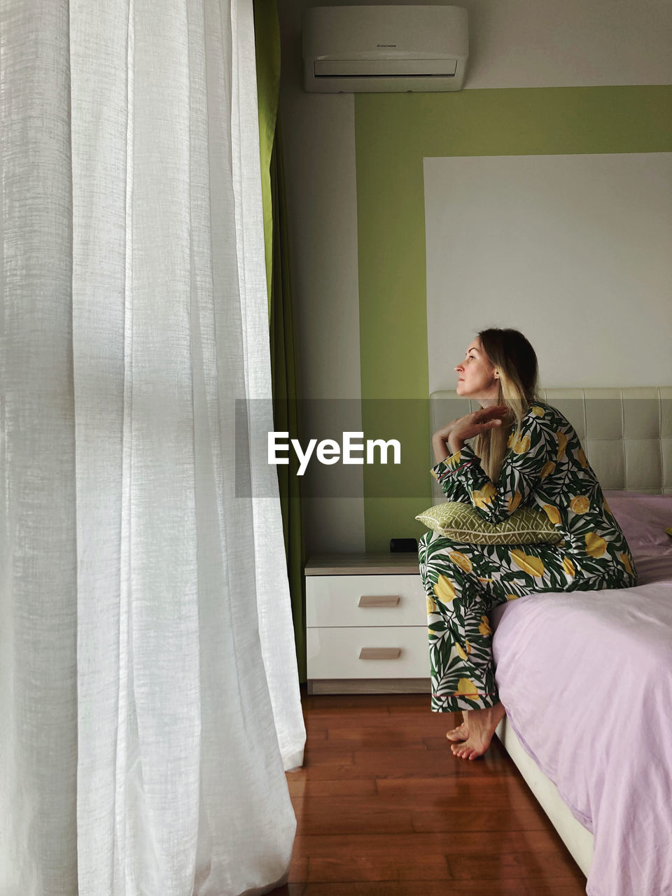 Side view of woman sitting on bed at home