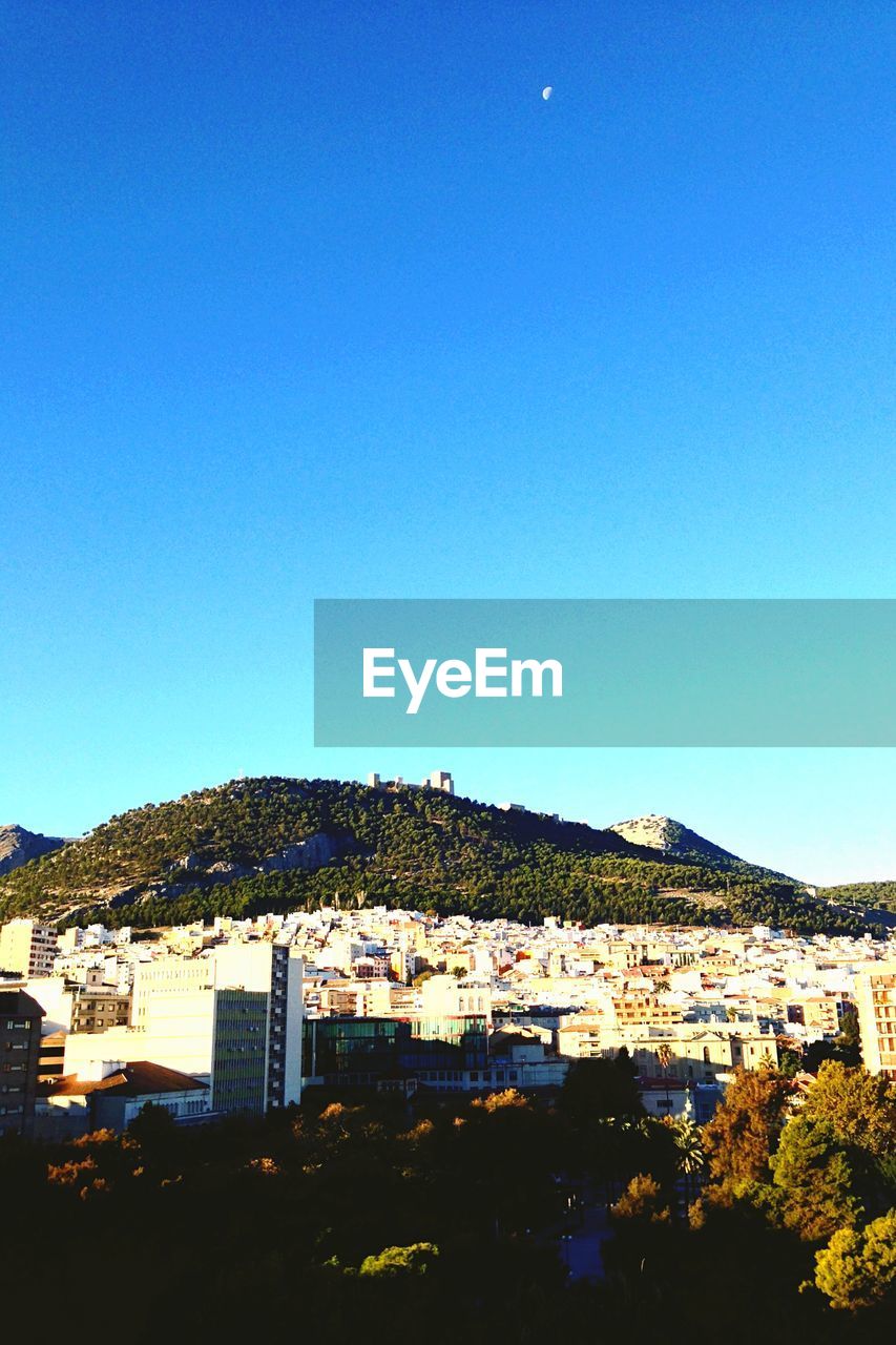 Buildings and mountains against clear blue sky