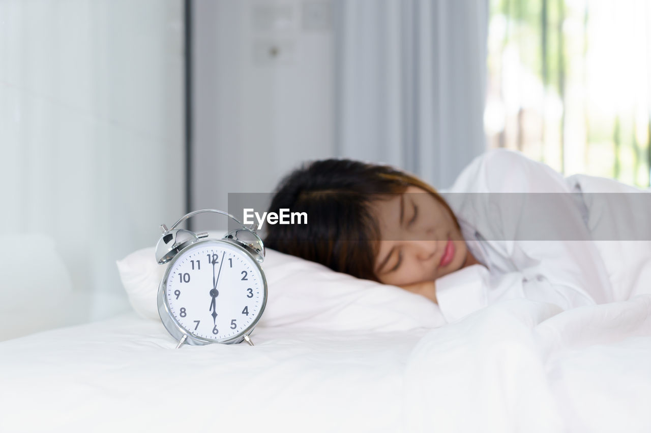 Woman sleeping by alarm clock on bed at home