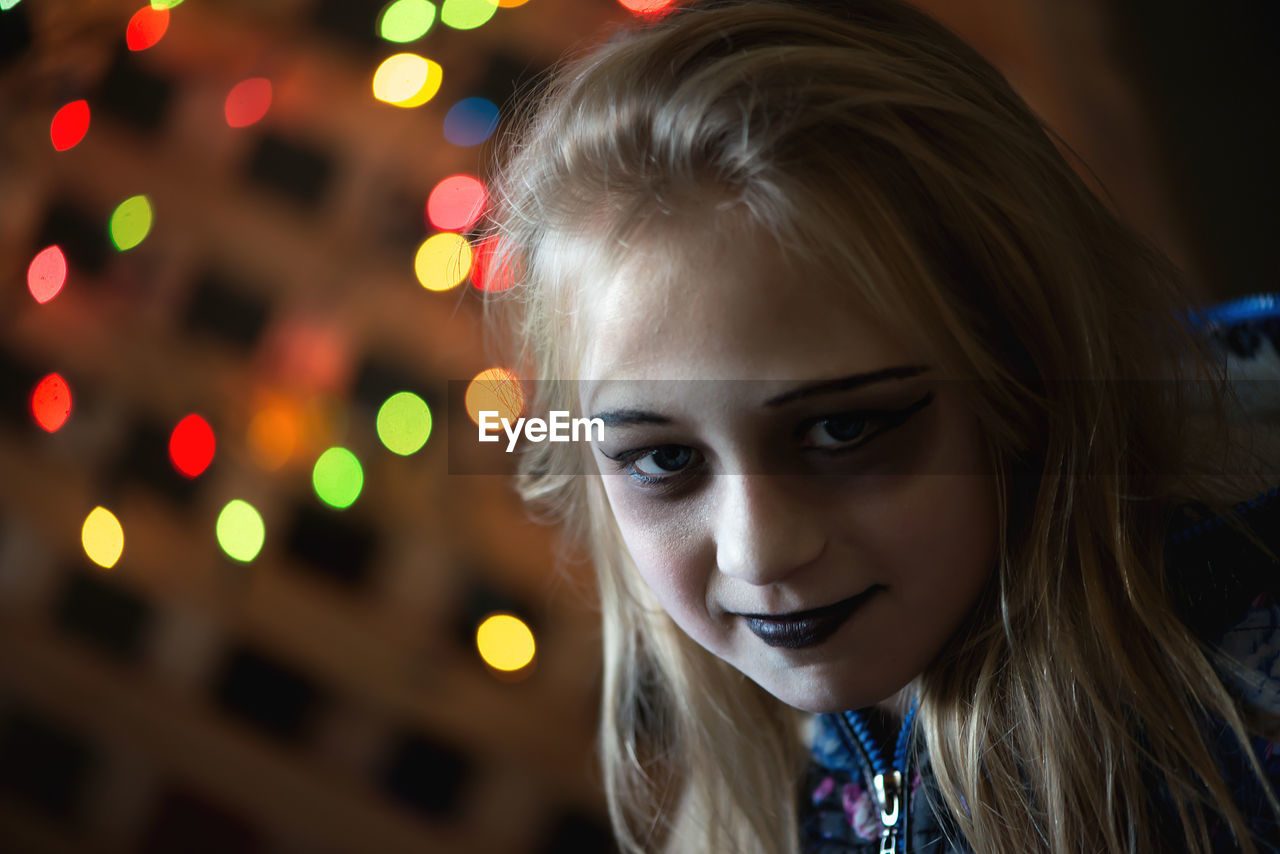 Close-up portrait of girl with halloween make-up against illuminated lights