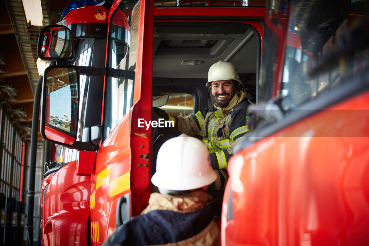 Smiling firefighter talking to coworker while sitting in fire truck at fire station