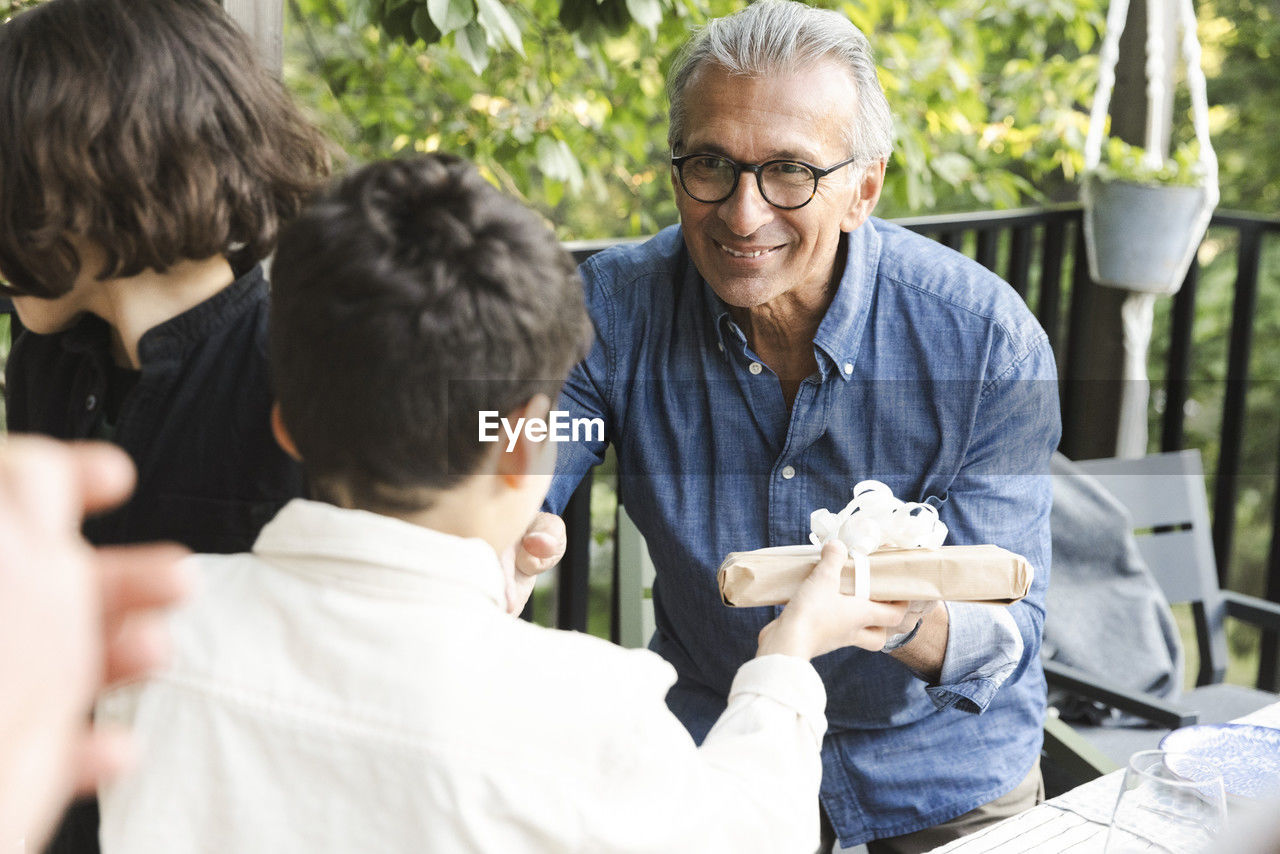 Smiling senior man giving gift to grandson during dinner party