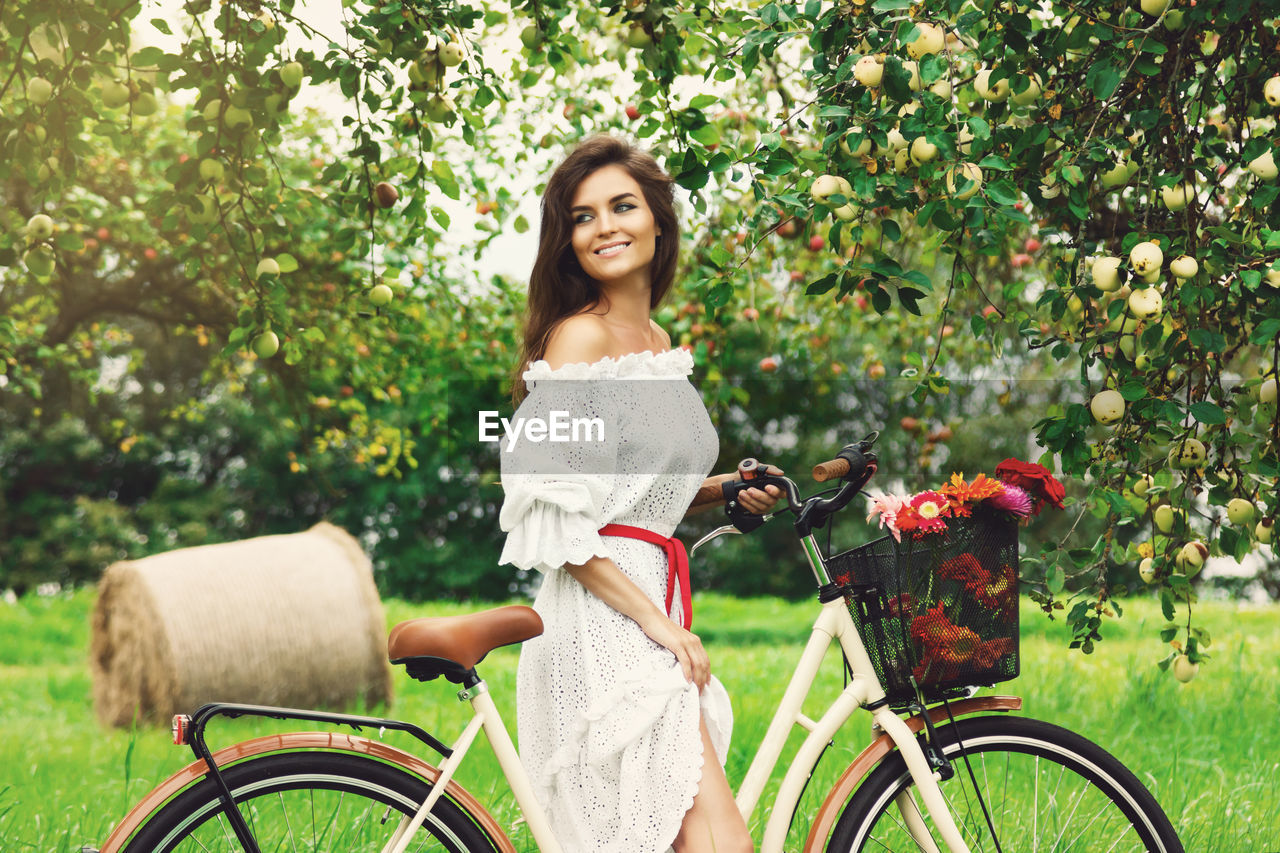 Smiling woman with bicycle at apple orchard