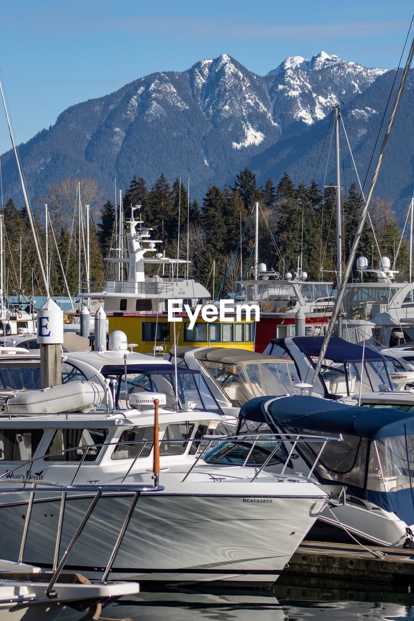 BOATS MOORED AT HARBOR AGAINST SNOWCAPPED MOUNTAINS