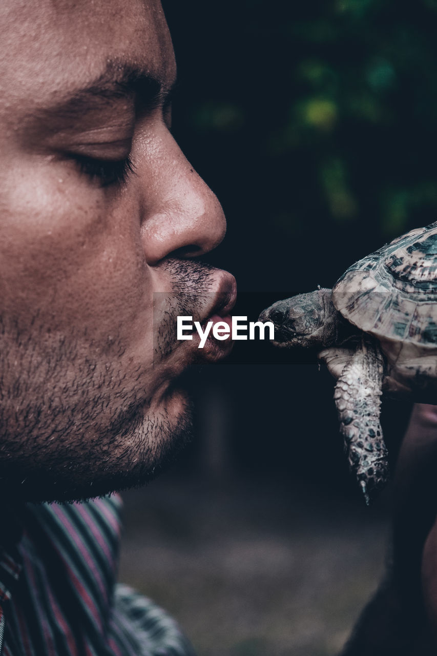 Side view of man kissing tortoise