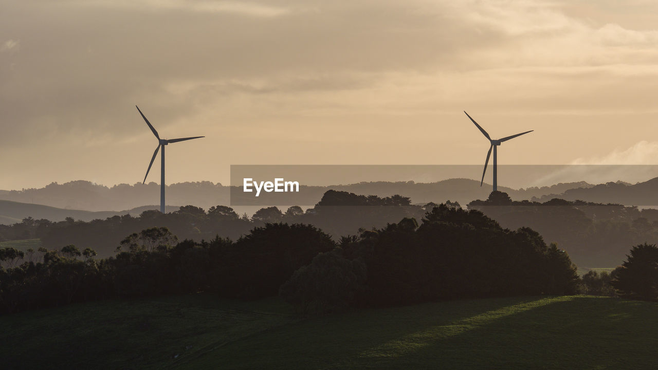 Wind turbines on field against sky during sunset