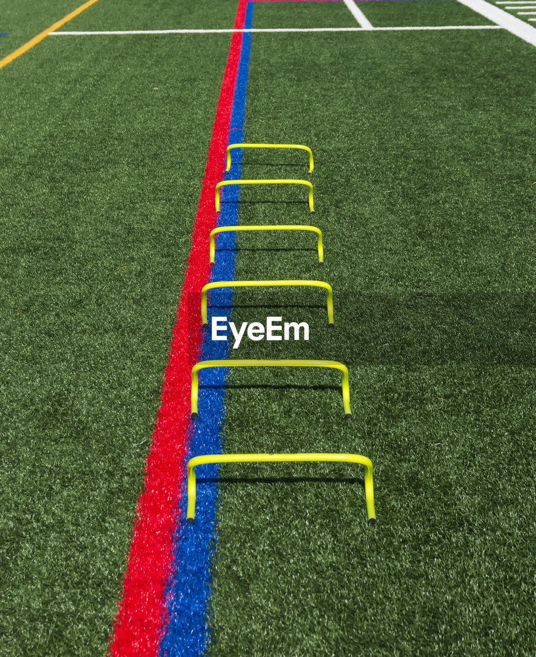 Six yellow mini hurdles lined up in a straight line on a turf field for speed and agility training.