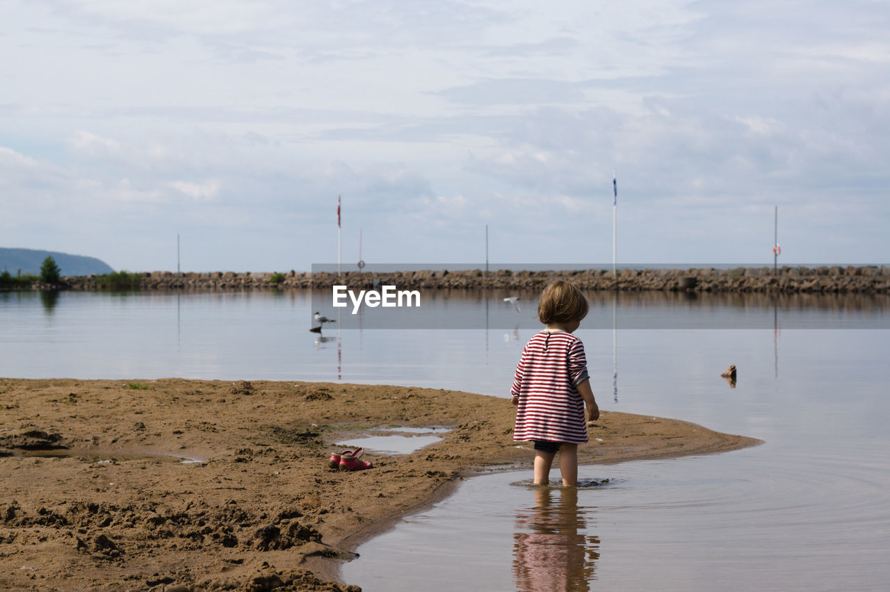 Rear view of girl standing in lake against cloudy sky