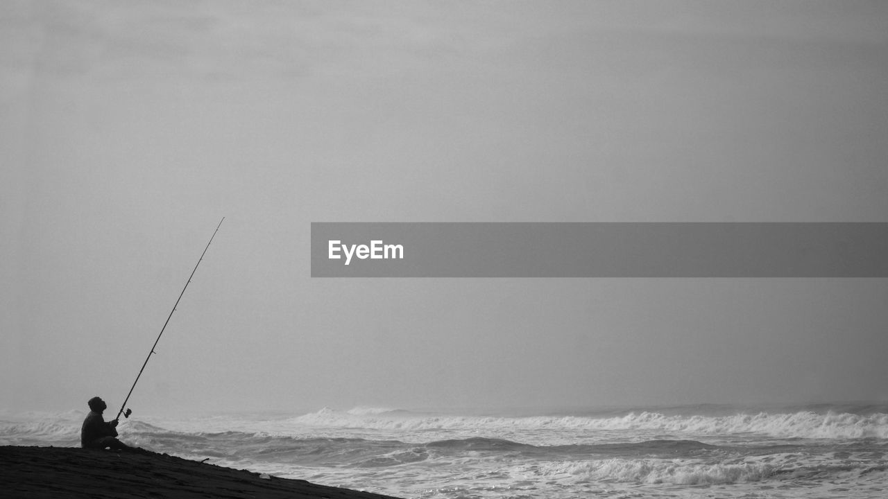 Silhouette of man fishing by the sea. sitting alone holding the long fishing rod.