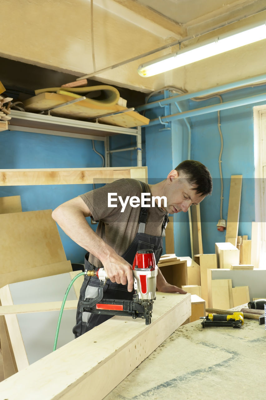 Stapling of wooden parts with a red pneumatic stapler. furniture manufacture. vertical format.