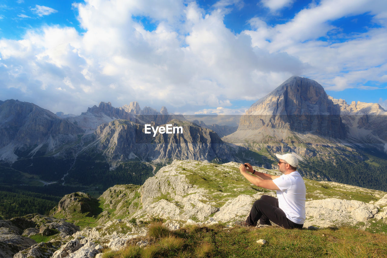 WOMAN SITTING ON MOUNTAIN AGAINST SKY