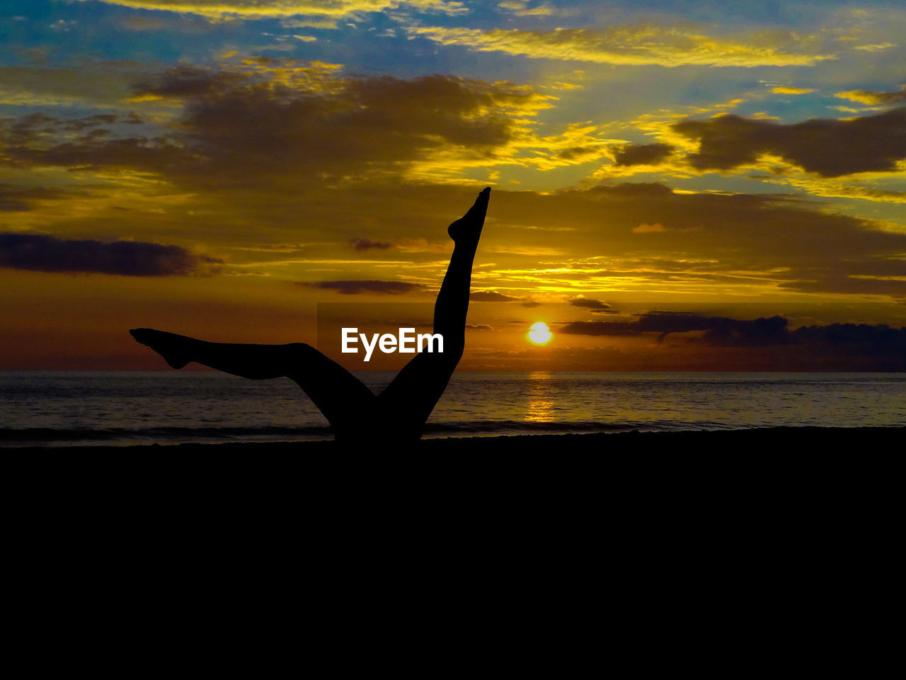 Silhouette woman at beach against cloudy sky during sunset