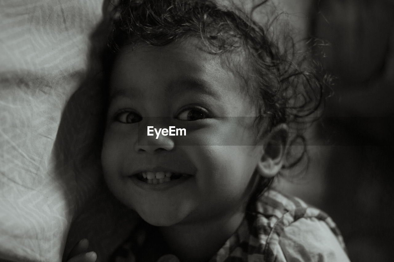 Close-up of cute smiling toddler lying on bed at home