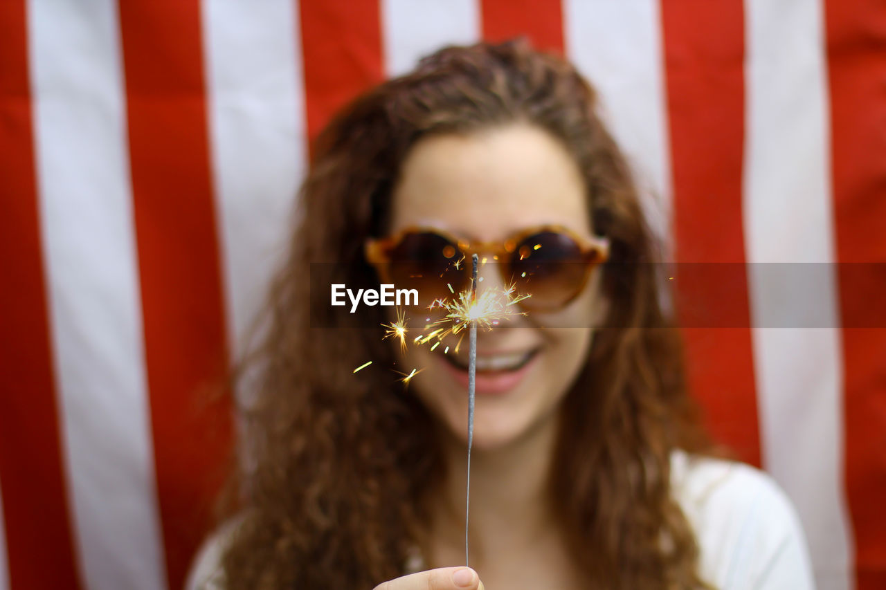  young redhead hispanic caucasian woman holding a sparkler standing in front of the american flag