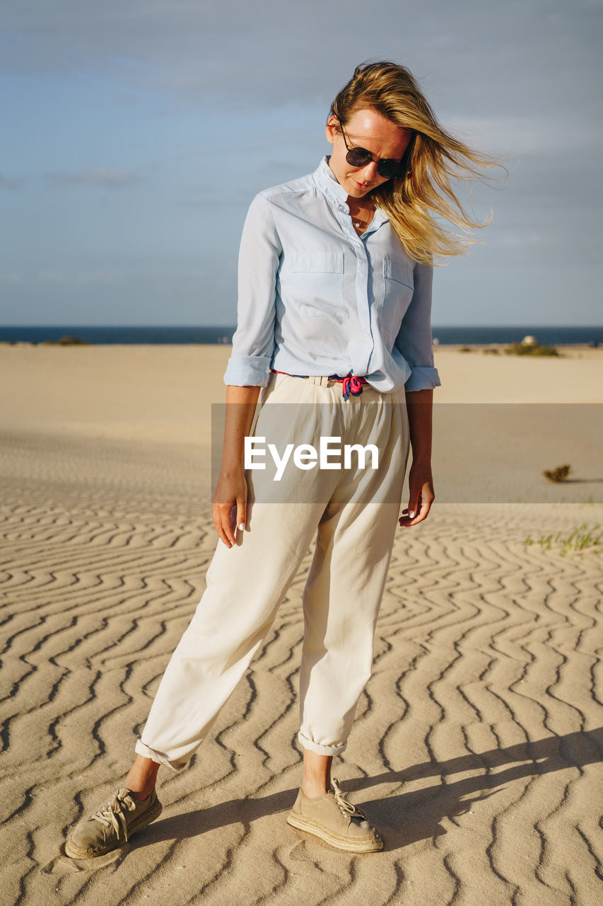 Young woman looking down while standing on sand at desert against sky