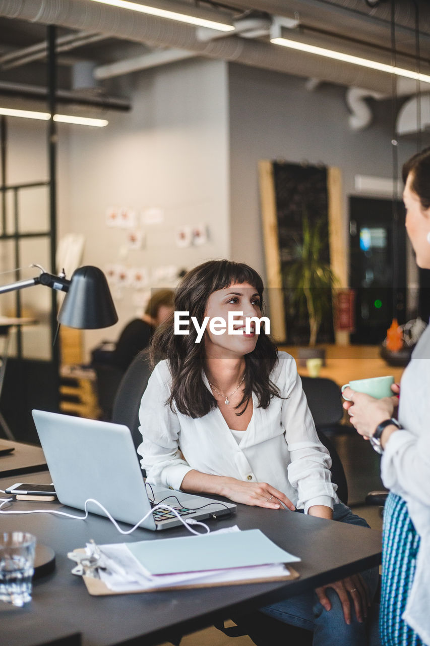 Female coworkers talking at desk in creative office