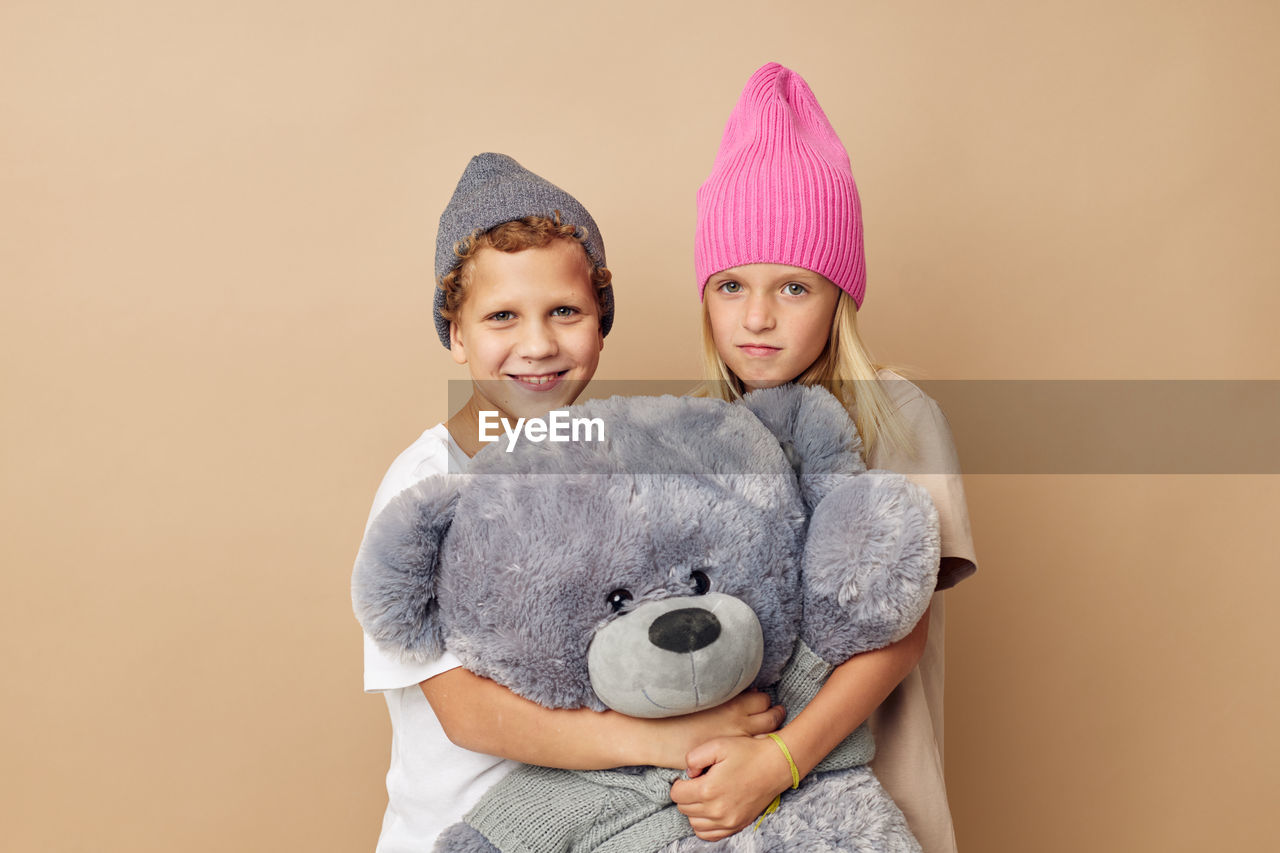 Portrait of sibling with stuffed toy against beige background