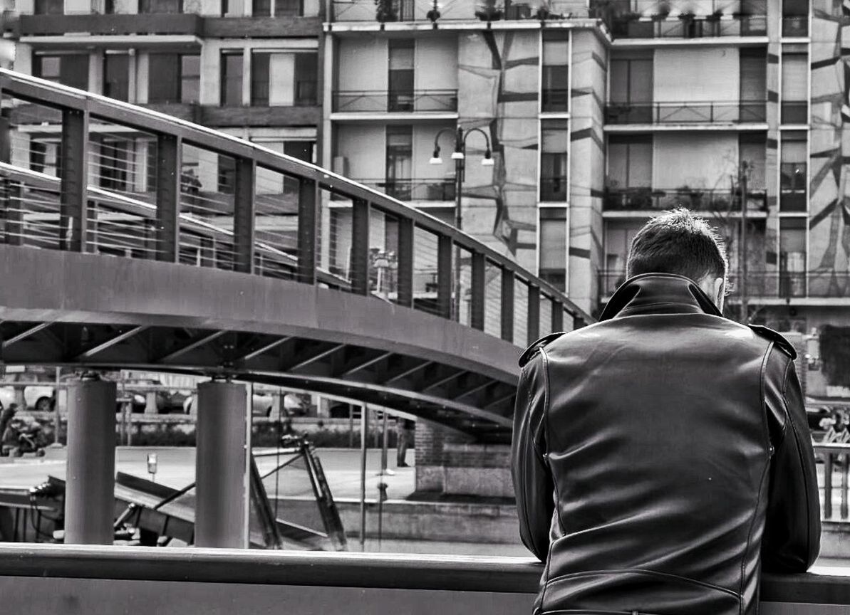 Rear view of man standing by bridge against building in city