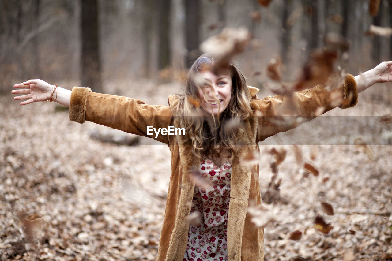 Cheerful young woman enjoying with autumn leaves on field