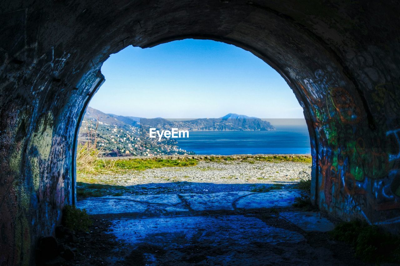 Arched structure on landscape with blue sea in background