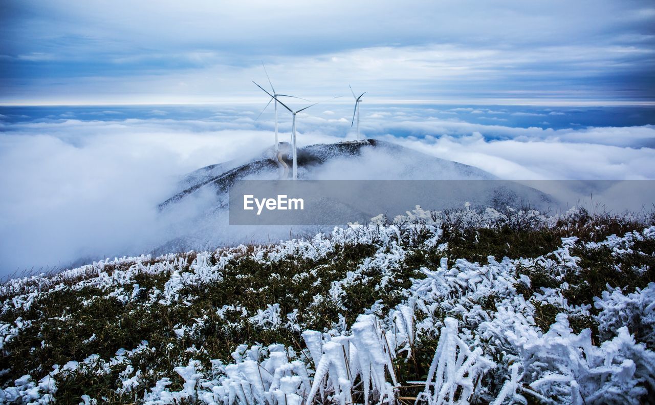 Windmills on mountain over clouds during winter