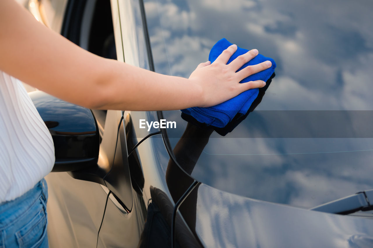 Midsection of woman cleaning car with blue textile outdoors