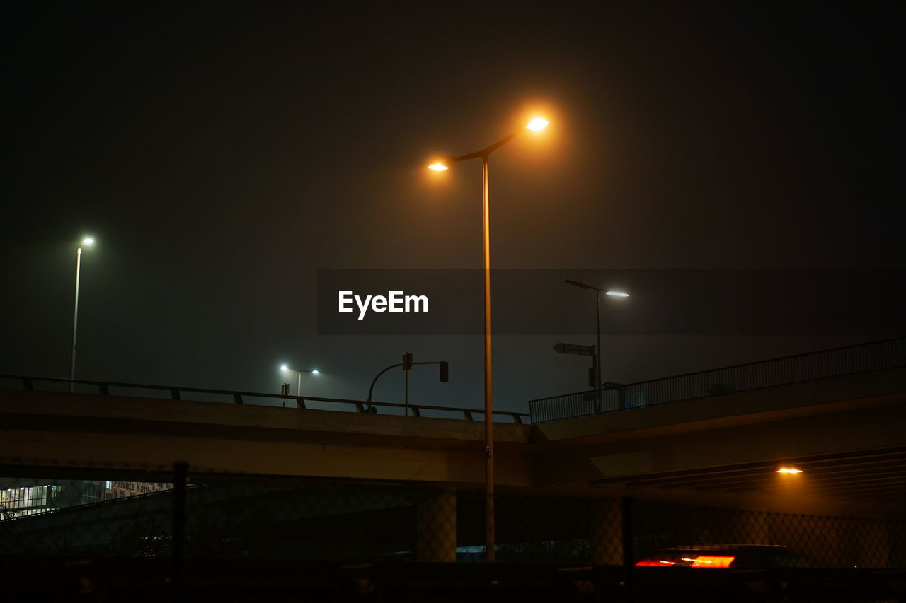 A motorway bridge from below at night with streetlights in the fog