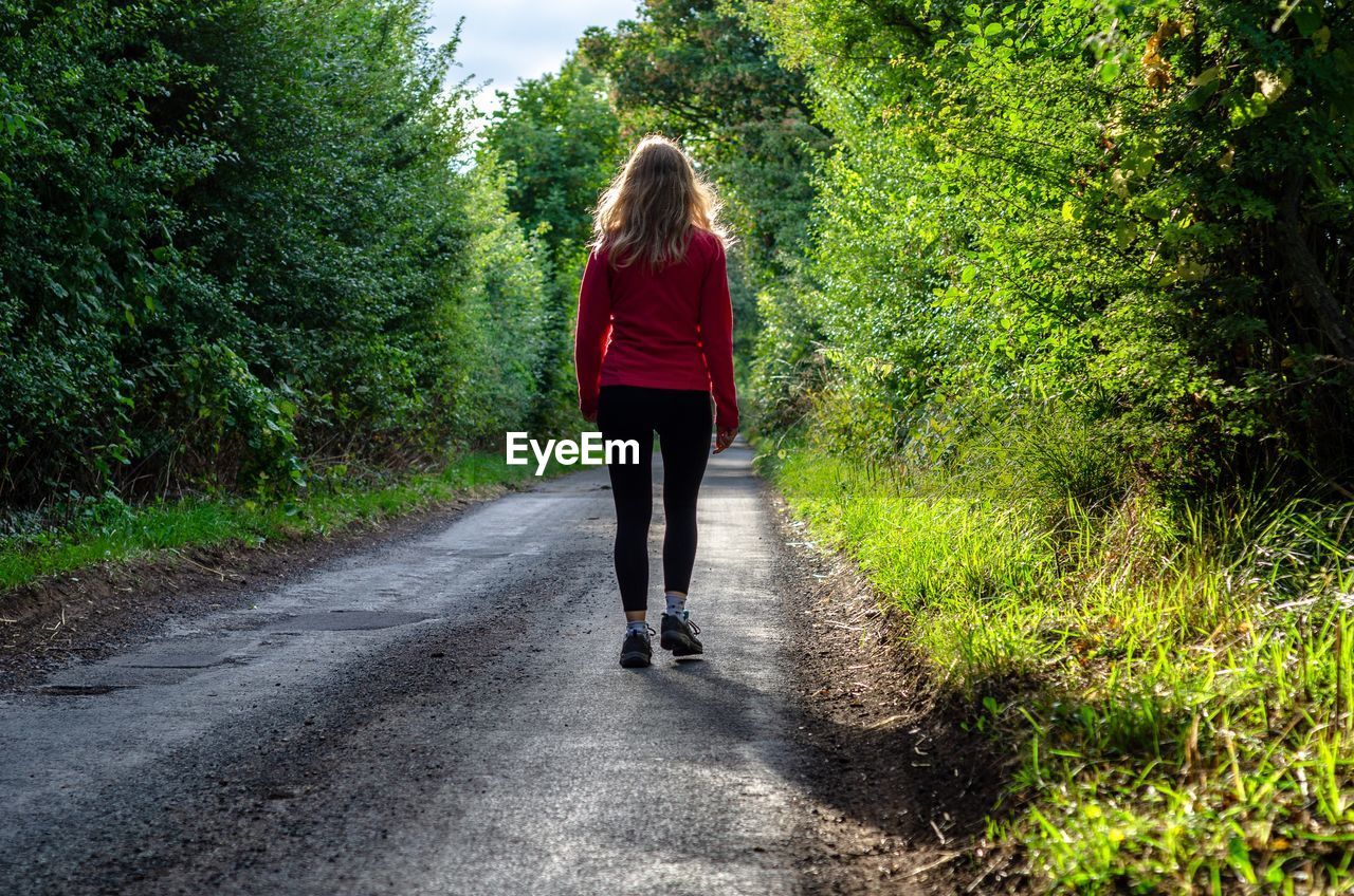 Rear view of woman walking on road amidst plants