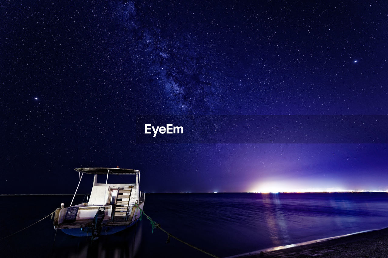 Boat moored at scenic illuminated sea against sky during night