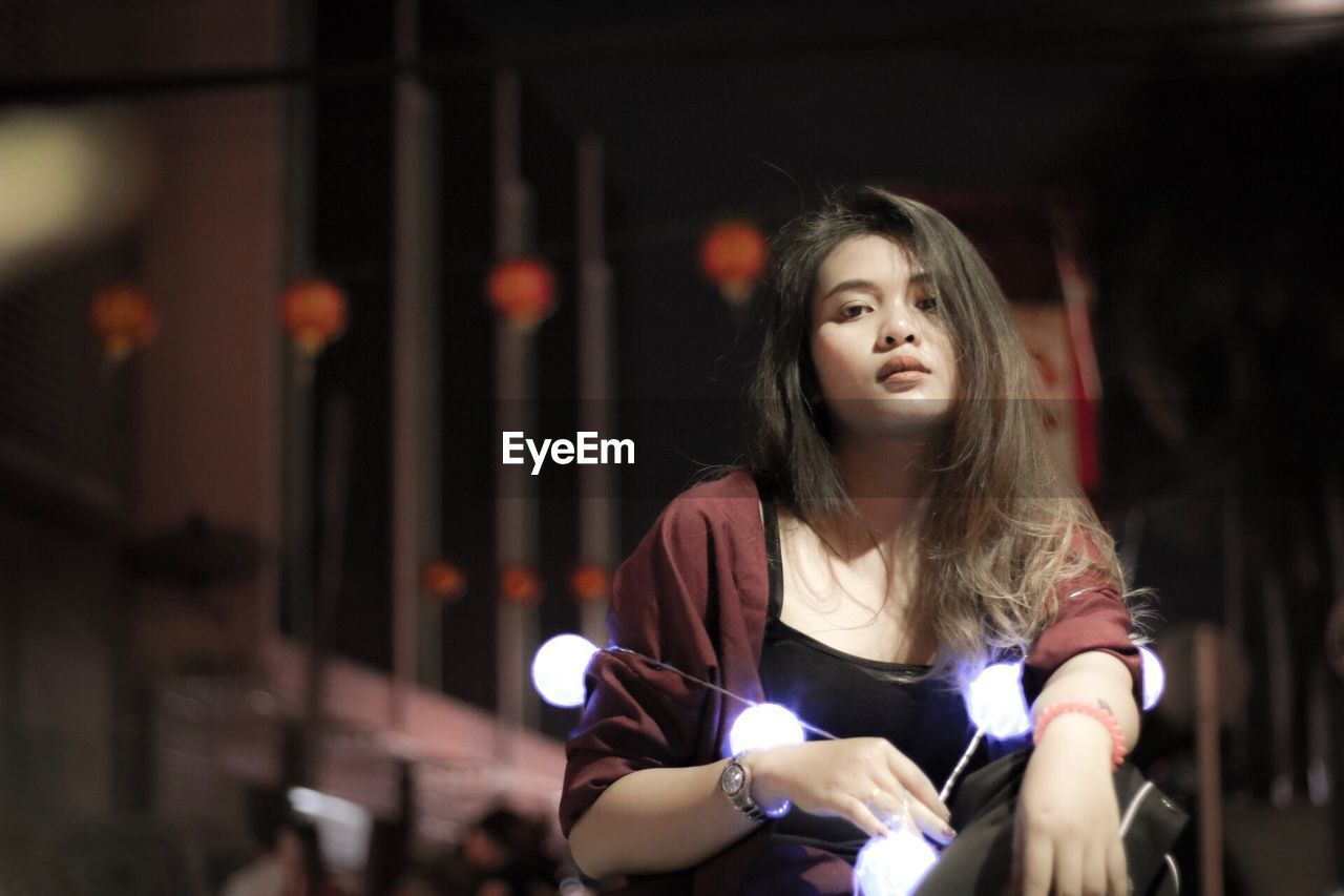 Portrait of beautiful young woman with illuminated lighting equipment at night