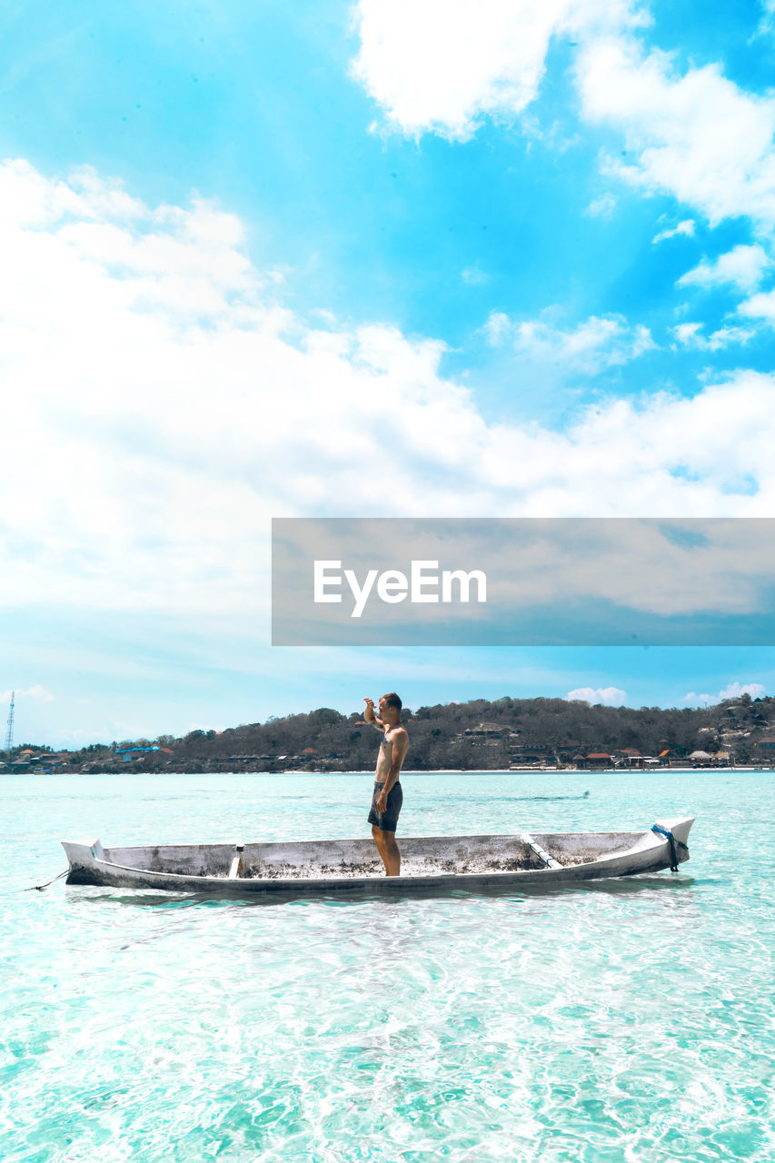 Man standing in boat on sea against sky