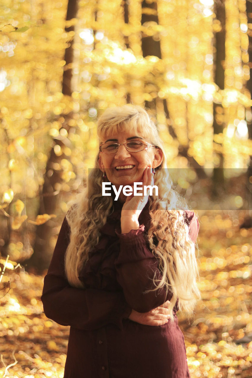 Portrait of a smiling senior woman with a long, grey hair, standing in the woods