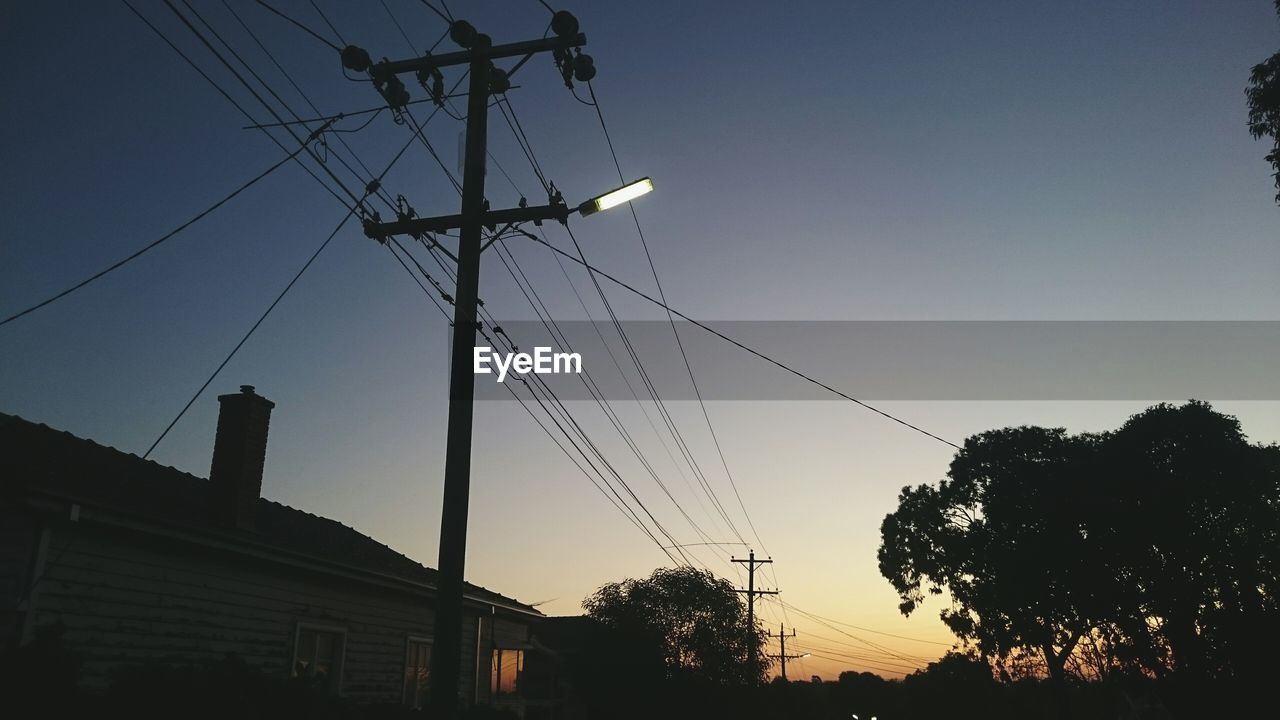 Low angle view of electricity pylon by house against clear sky