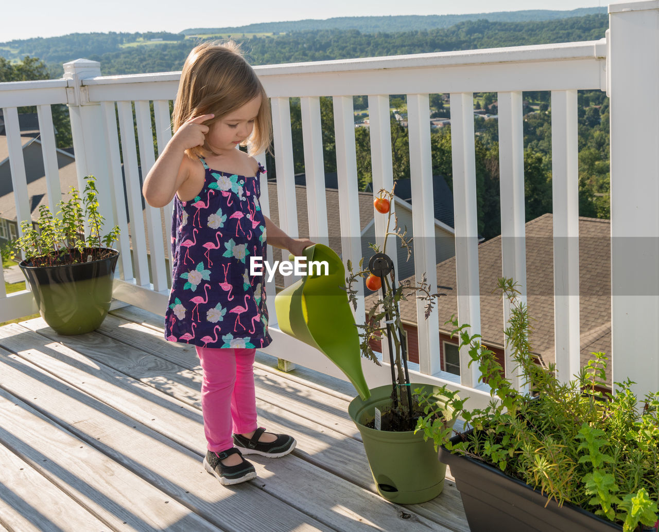 Girl with leaves standing by potted plants at balcony