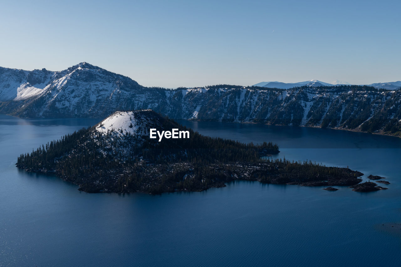 Scenic view of crater lake and wizard island against blue sky with snow