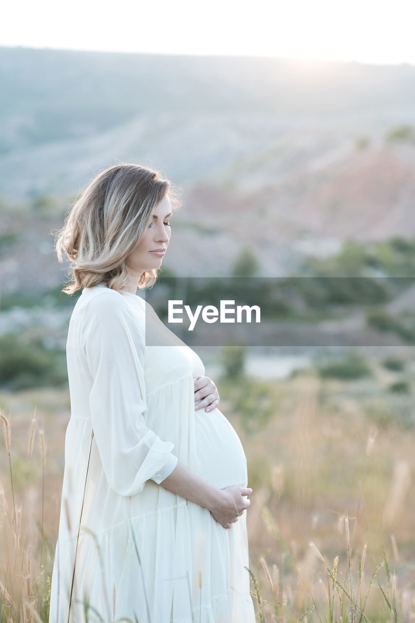 Pregnant woman holding belly standing on field