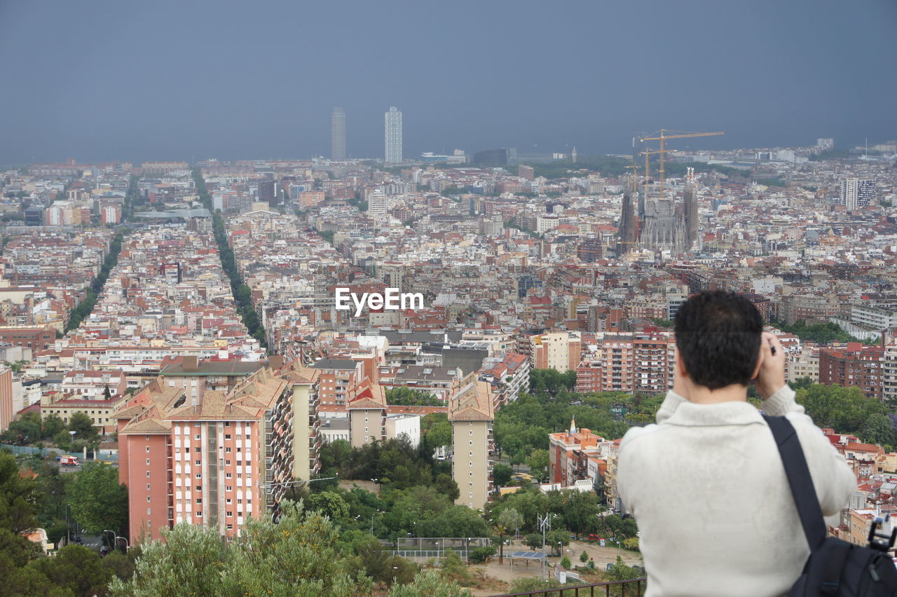 Rear view of man photographing sagrada familia amidst cityscape
