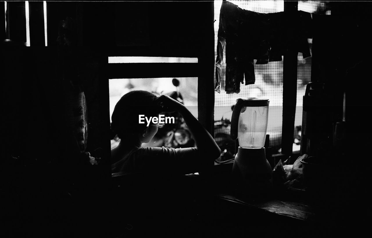 Rear view of woman sitting by window in darkroom