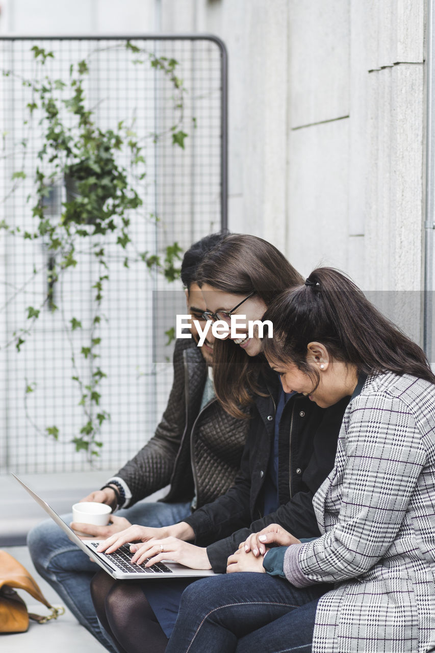 Smiling male and female business professionals working over laptop while sitting in office