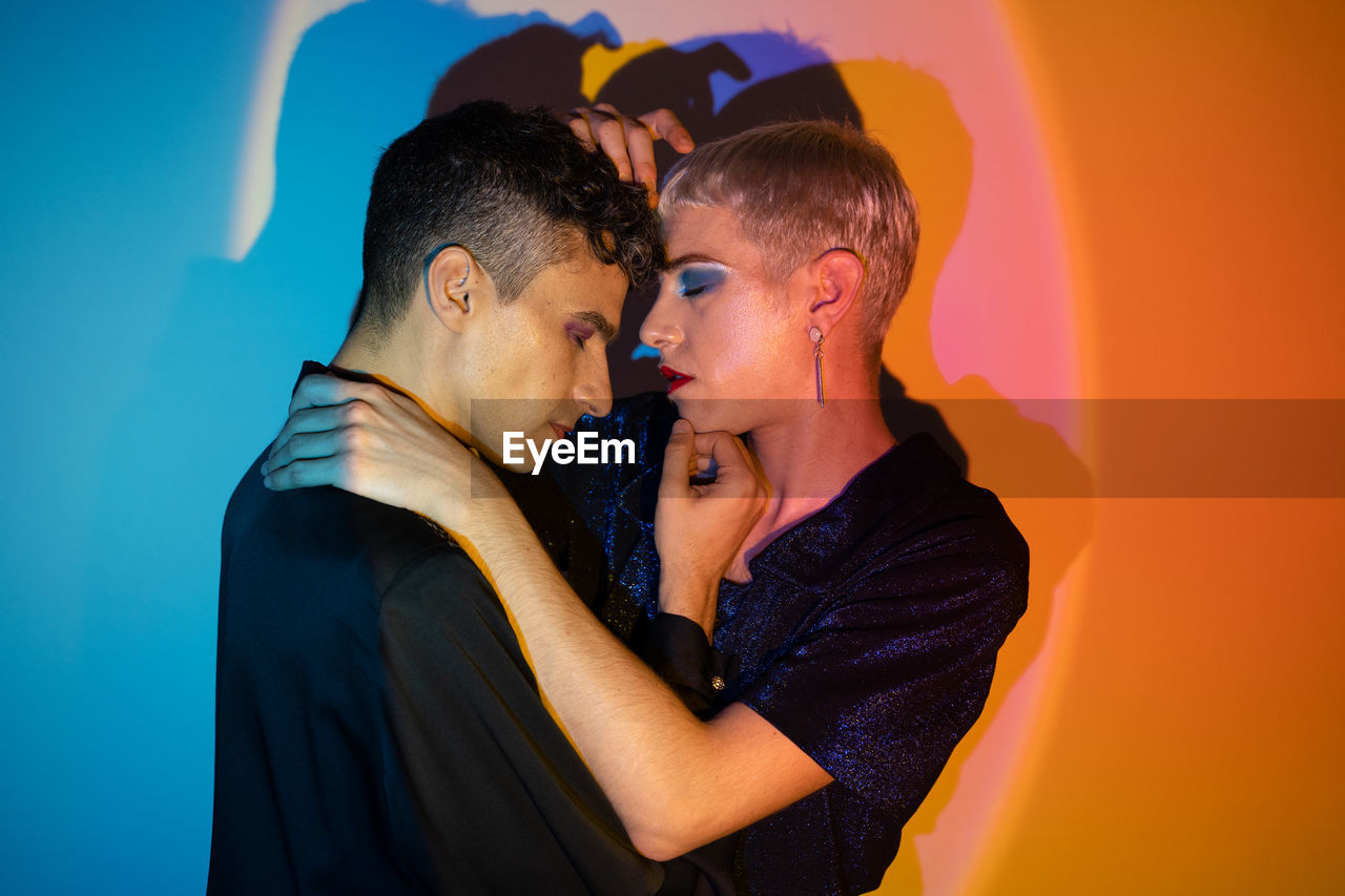 Portrait of gay couple wearing makeup and embracing in illuminated studio