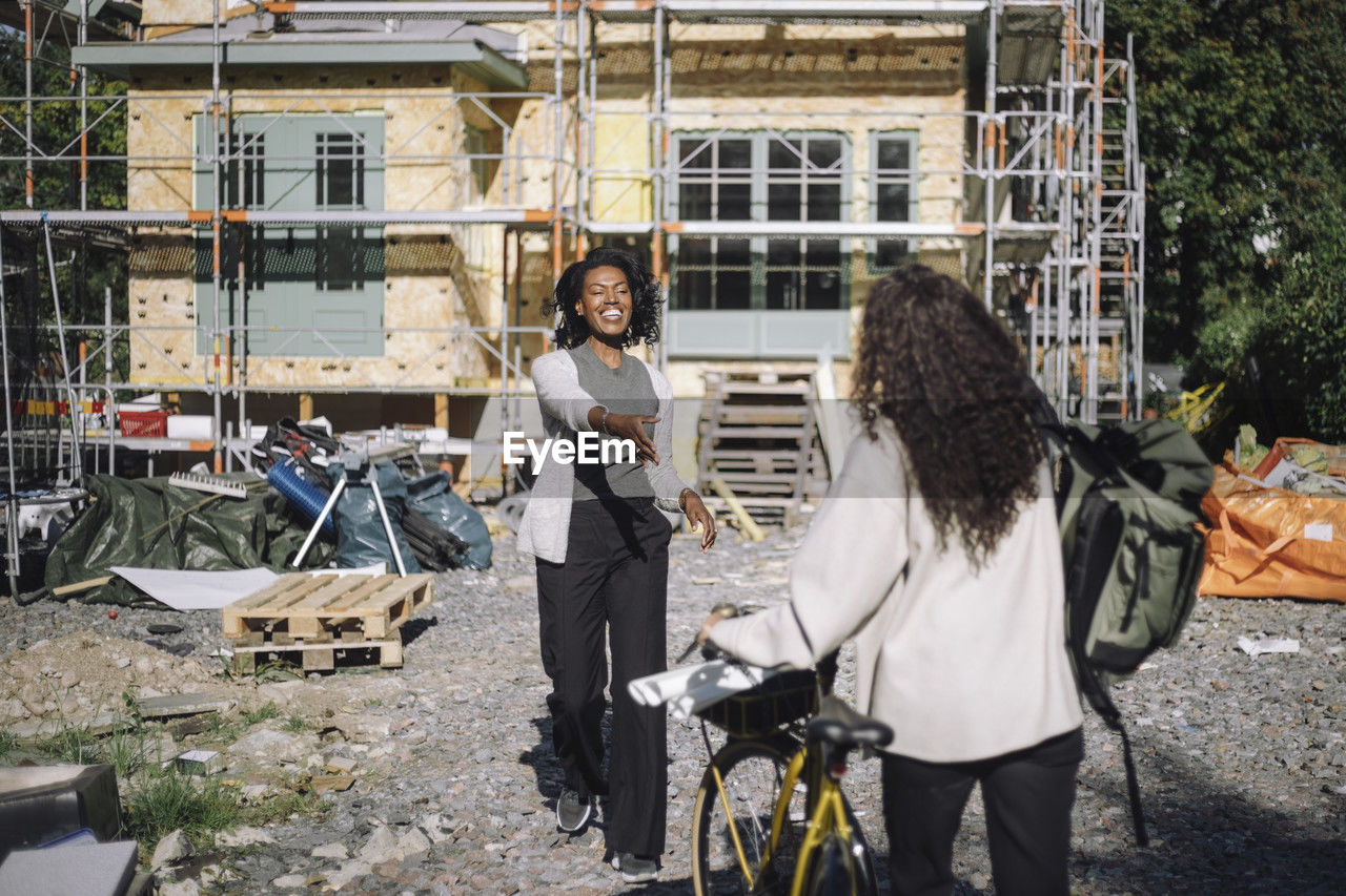 Smiling customer greeting female architect arriving with bicycle at construction site