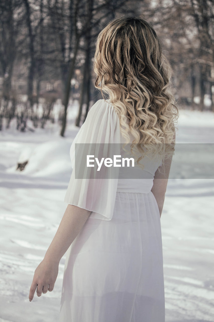 Rear view of young woman while standing on snow covered field