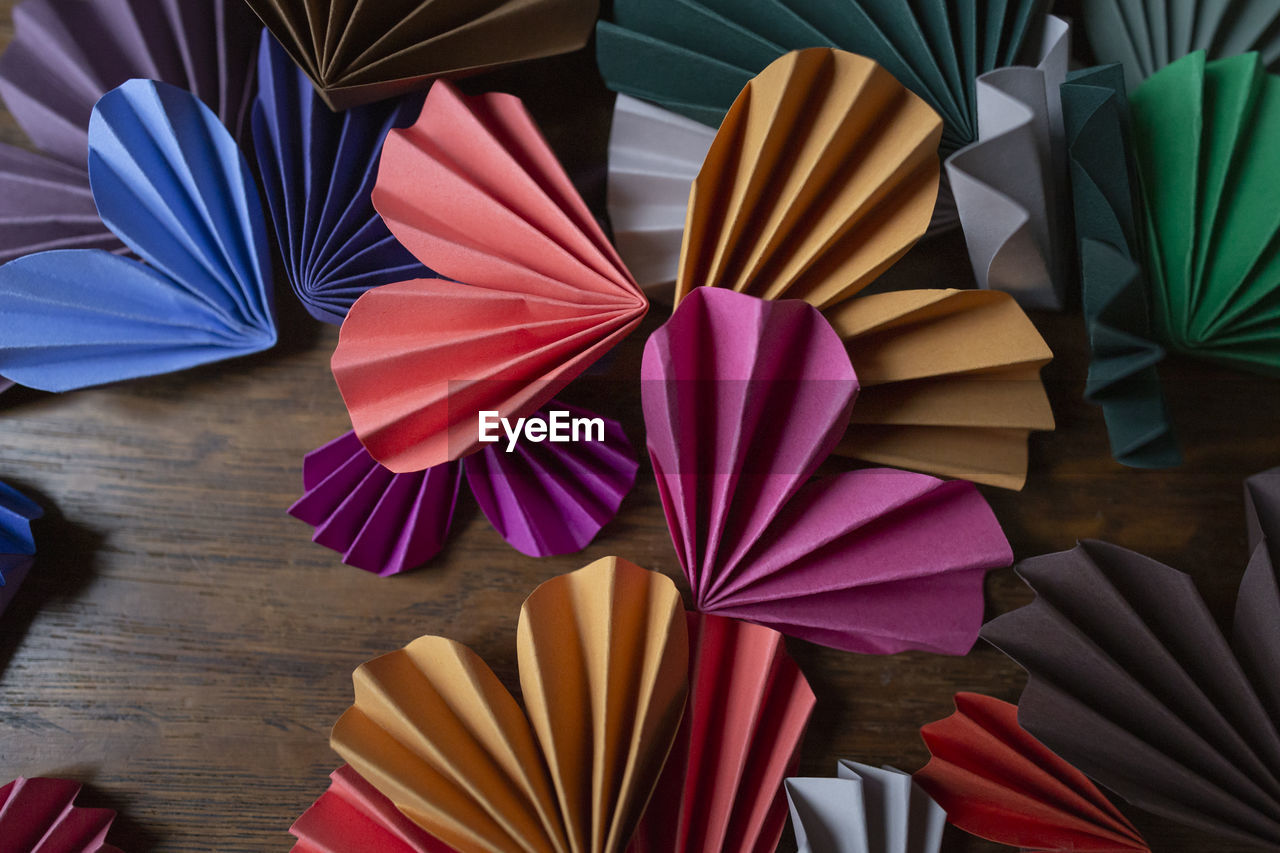 Top view of colorful handmade paper hearts arranged on wooden surface