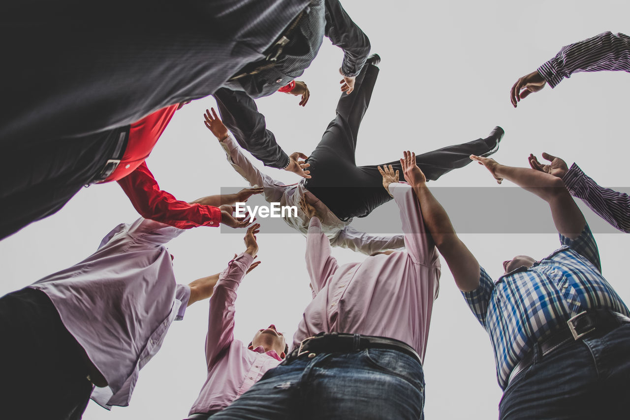 Low angle view of men throwing bridegroom against clear sky