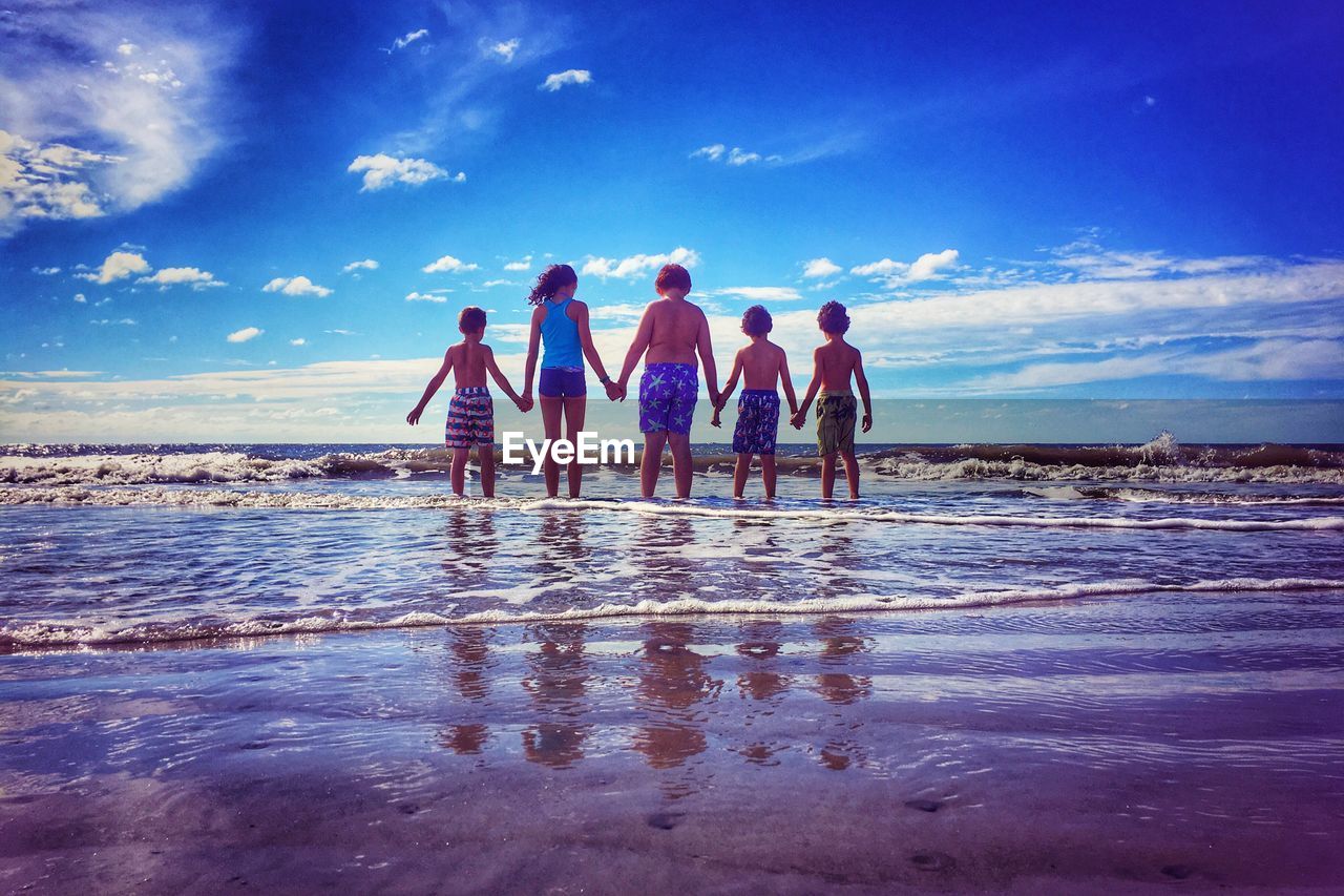 REAR VIEW OF PEOPLE AT BEACH AGAINST SKY