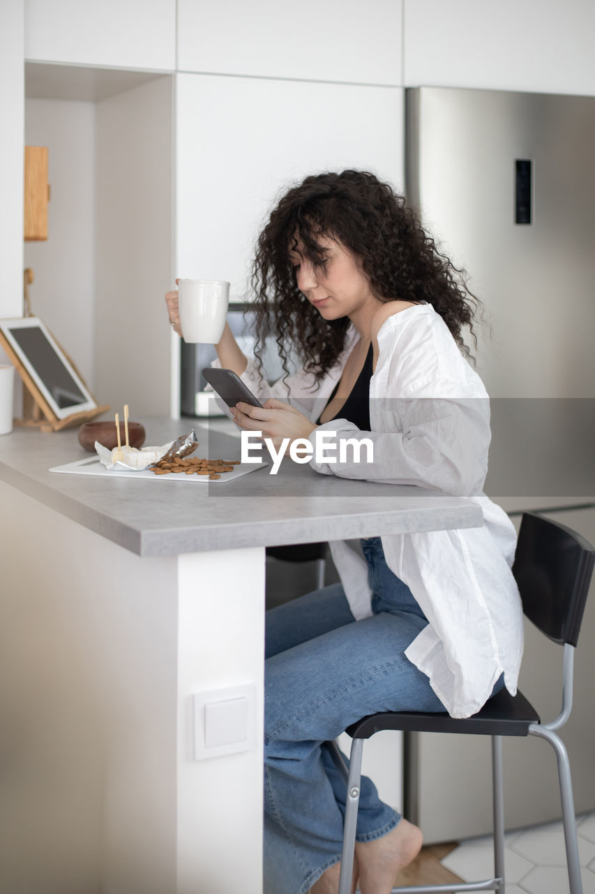 Side view of woman using phone while sitting on table