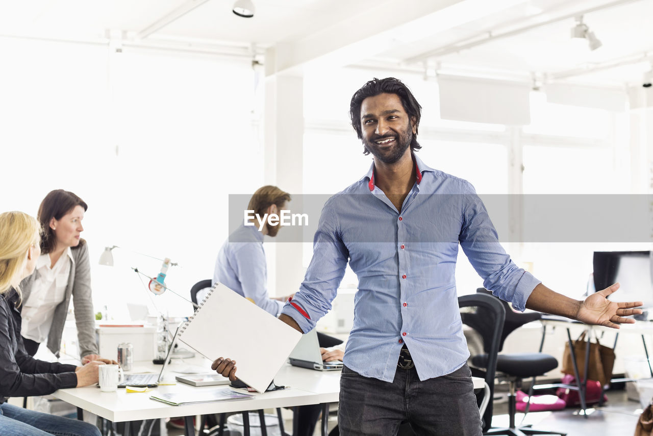 Mid adult businessman standing with arms outstretched in office
