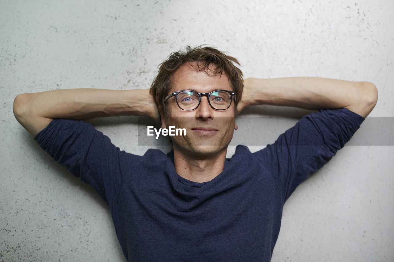 Portrait of smiling man with hands behind head wearing glasses